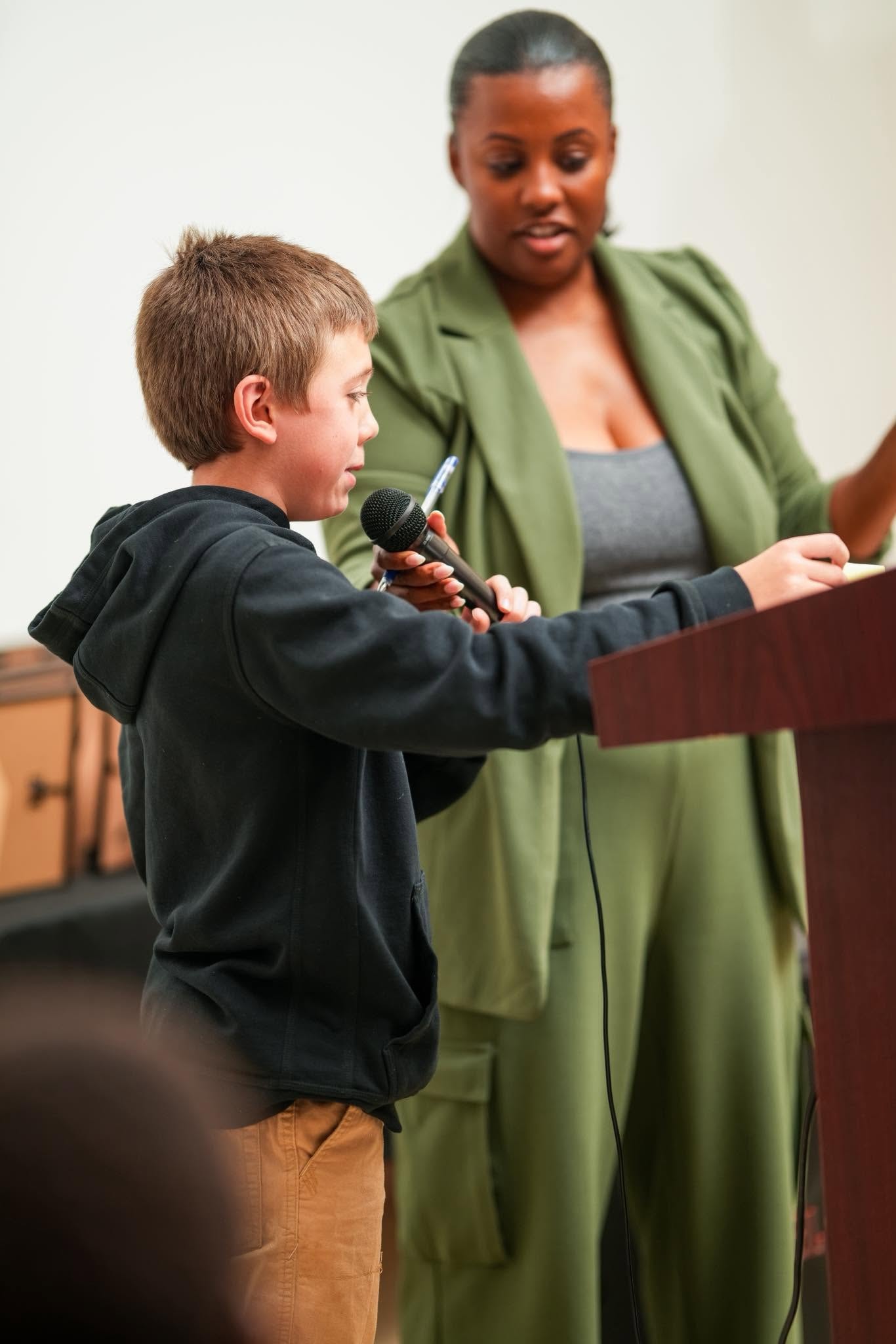 Boy speaking into a microphone with a teacher